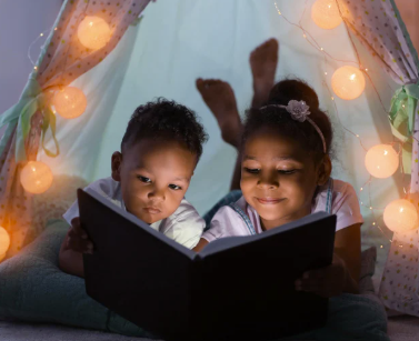 Zwei Kinder lesen gemeinsam ein Buch im Zelt